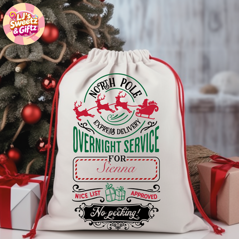 Personalized Christmas gift sack with Santa Claus design and text, placed in front of a decorated Christmas tree.