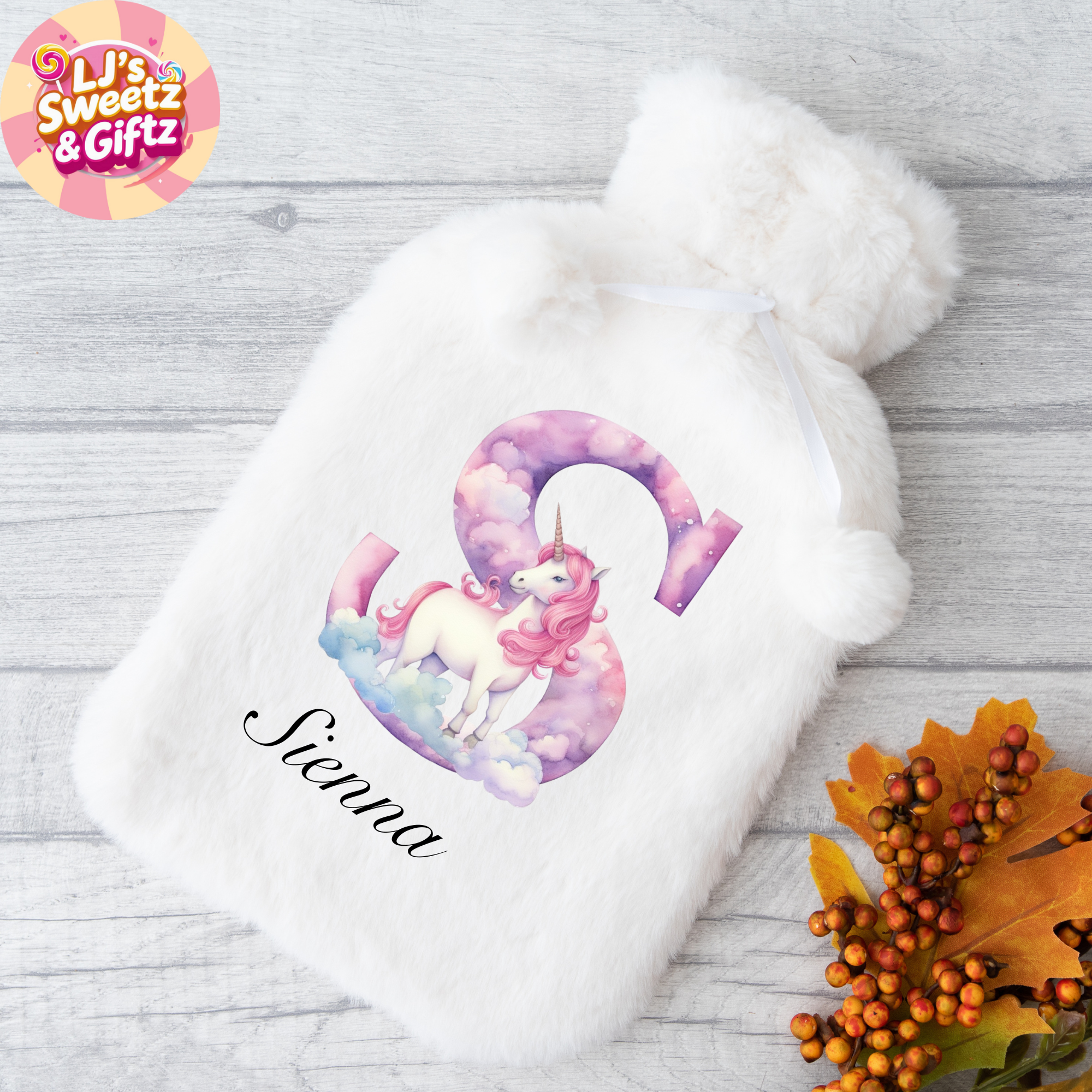 White hot water bottle with unicorn design and 'Sienna' text on a wooden surface with fall leaves.