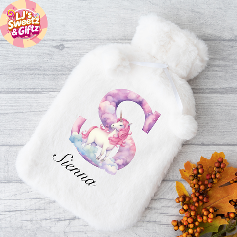 White hot water bottle with unicorn design and 'Sienna' text on a wooden surface with fall leaves.