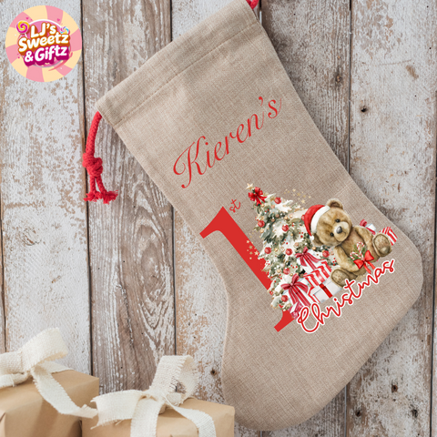 Beige Christmas stocking with teddy bear and tree design, featuring the text 'Kieren's 1st Christmas', on a wooden background.