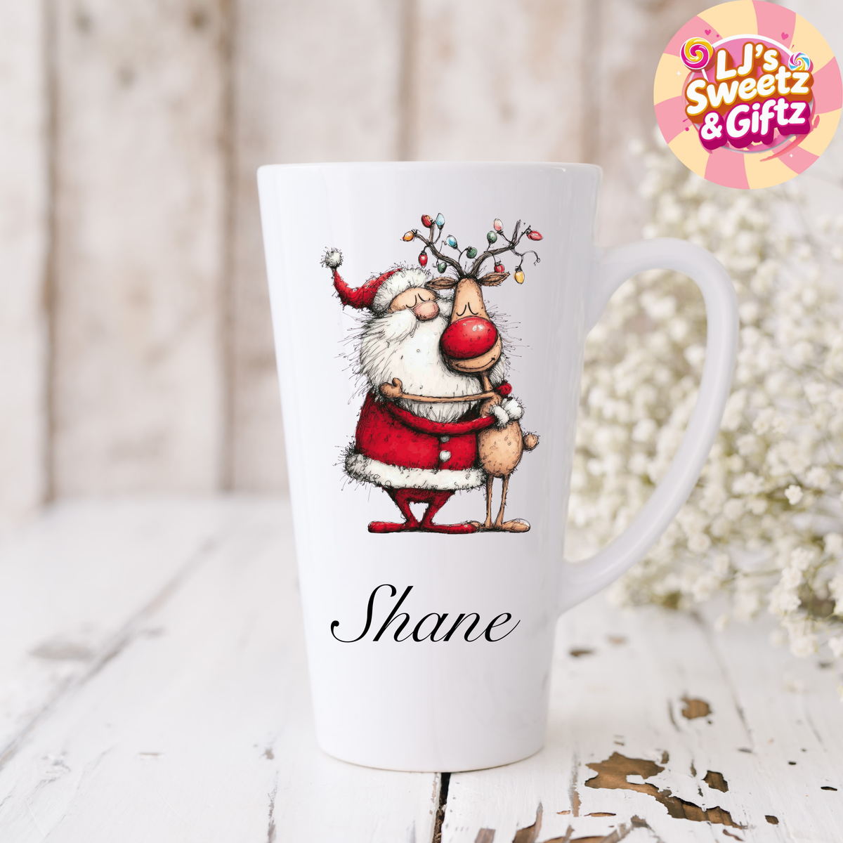 White mug with a Christmas-themed design of a reindeer wearing a Santa hat, on a light wooden surface with a blurred background.
