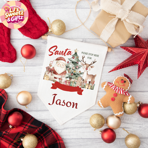 Personalized Christmas sign with Santa and reindeer design, surrounded by festive decorations on a wooden surface.