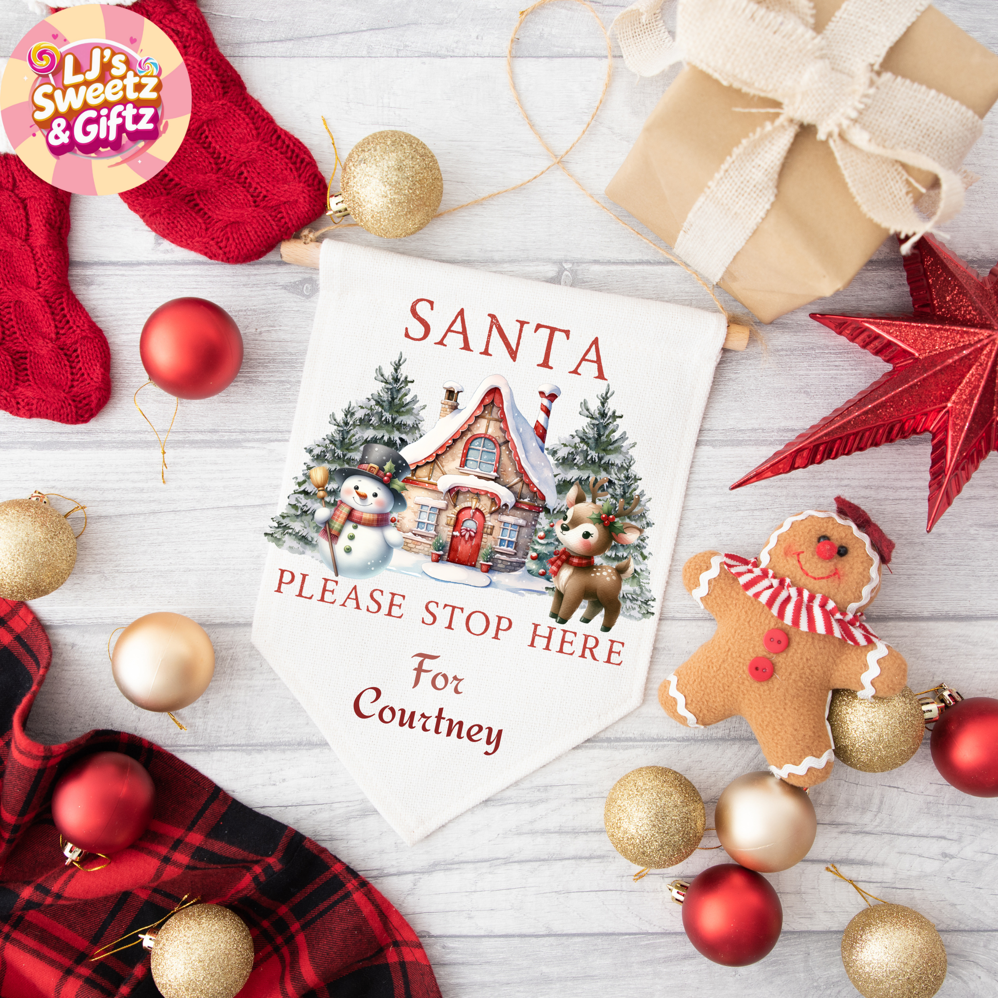 Personalized Christmas sign with Santa please stop here text, surrounded by festive decorations on a wooden surface.