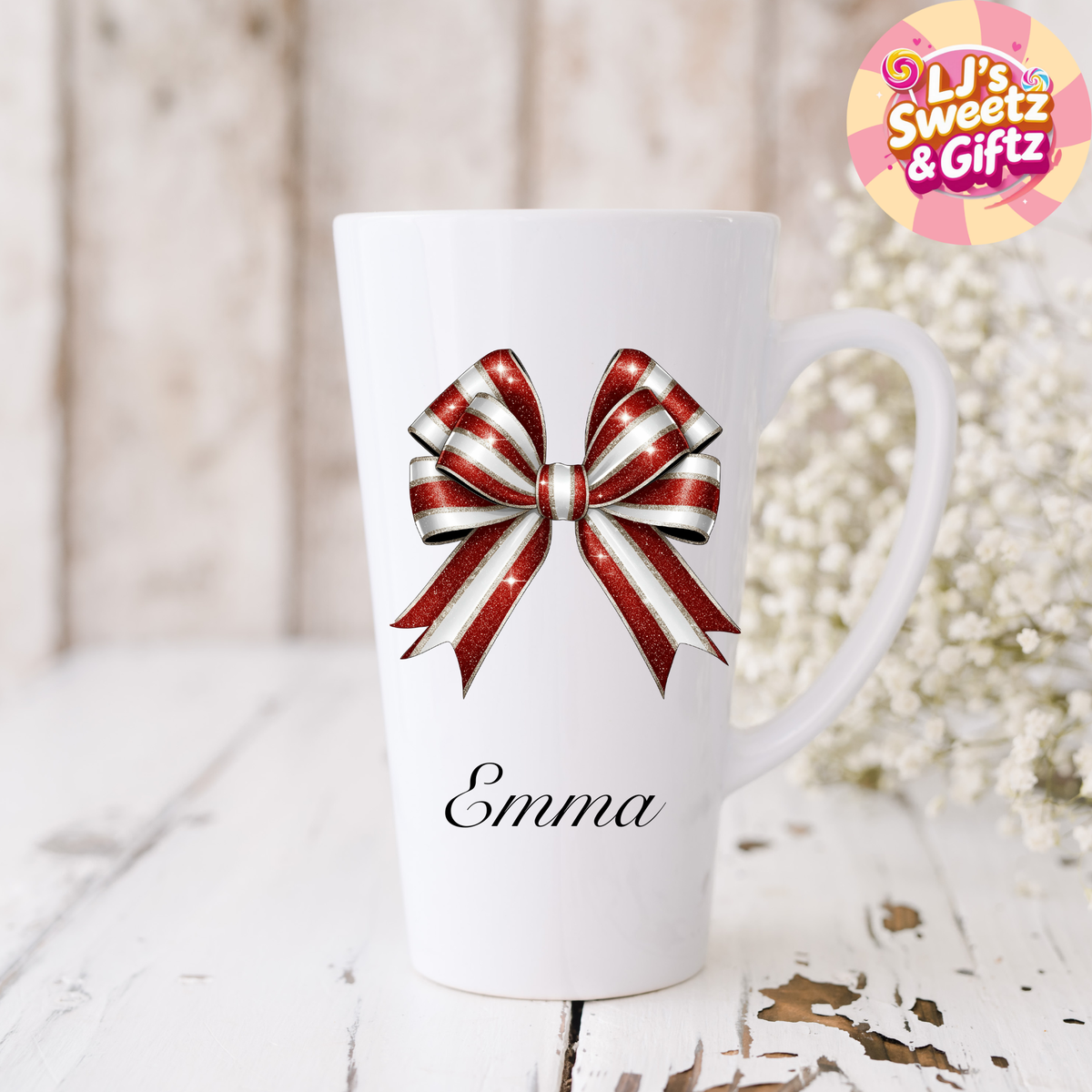 White mug with a red and white bow design and the name 'Emma' on a light wooden surface.