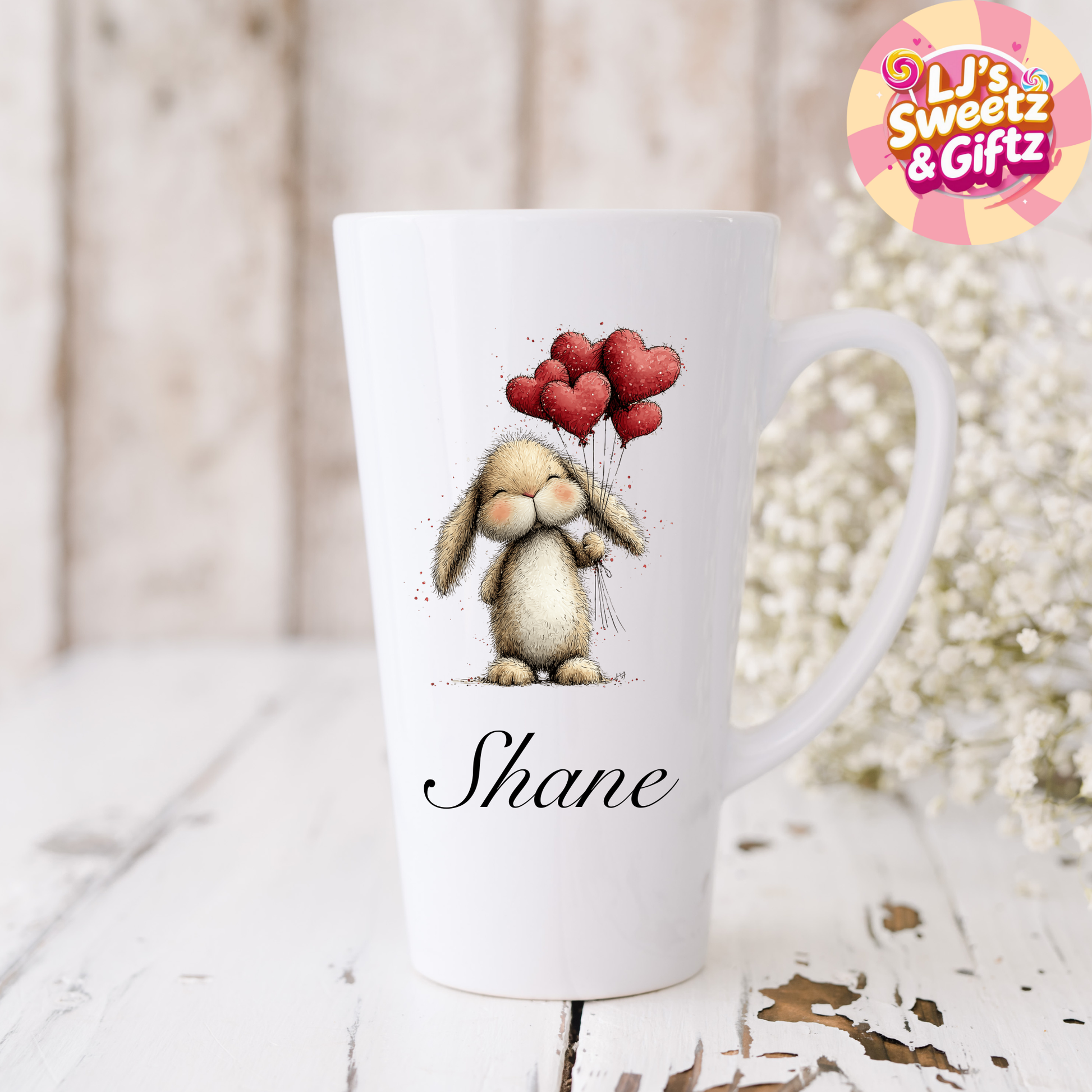 White mug with a bunny holding heart-shaped balloons design, personalized with 'Shane', on a wooden surface with decorative elements.